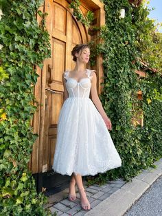 a woman standing in front of a door wearing a white dress