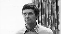 a black and white photo of a man wearing a shirt and tie with an american flag in the background