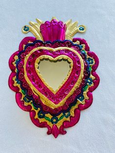 a heart shaped mirror is hanging on the wall in front of a white background with blue, yellow and pink accents