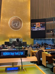 people are sitting at desks in the united states assembly building, with large screens above them