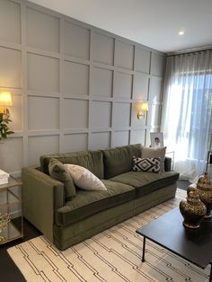 a living room with green couches and white wall paneling on the walls behind them