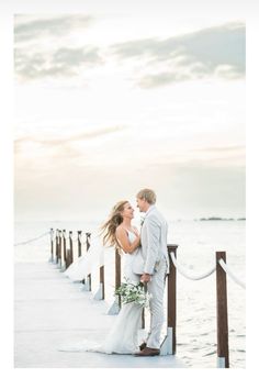 a bride and groom standing on a pier in front of the ocean at their wedding