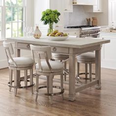 a kitchen island with four chairs and a bowl of fruit on the table in front of it