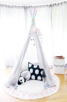 a teepee tent in the corner of a room with white curtains and black and white pillows