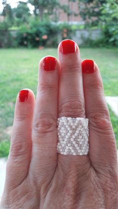 a woman's hand with red nail polish and a ring on her finger, in front of a grassy area