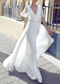 a woman in a white dress is walking down the street with her hand on her hip