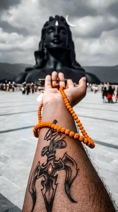 a person with a tattoo on their arm holding a beaded bracelet in front of a statue