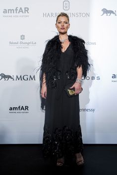 a woman in a long black dress and feathered jacket on the red carpet at an event