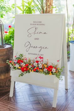 a welcome sign with flowers and greenery on the side for an outdoor wedding ceremony