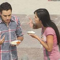 two people are standing outside eating food from plates and talking to each other with their hands in the air