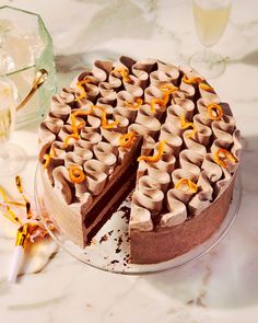 a chocolate cake with slices missing from it on a table next to glasses and utensils