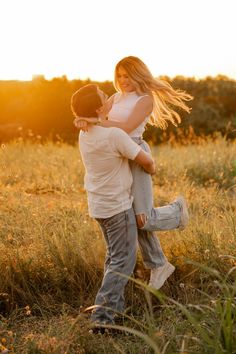 a man and woman hug in the middle of a field with tall grass at sunset