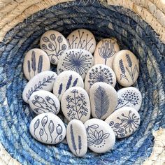 some rocks with designs on them in a blue and white woven basket filled with straw