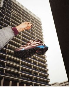 a person holding up a shoe in front of a tall building