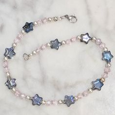 a necklace with blue and white stars on it sitting on a marble counter top next to a beaded bracelet