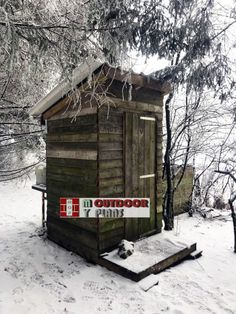 a small wooden outhouse in the middle of snow covered ground with trees behind it