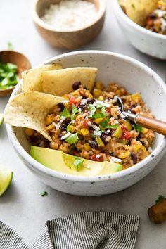 two bowls filled with mexican rice, beans and avocado garnished with tortilla chips