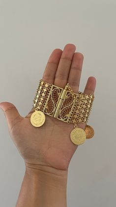 a hand is holding two gold bracelets with coins on them, and the other one has