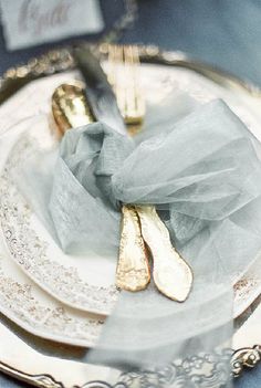 two silver and gold utensils sitting on top of a white plate with lace