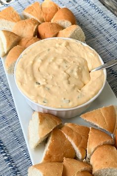 a white plate topped with bread and dip next to rolls on a blue table cloth