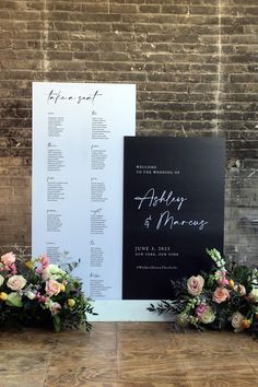 the wedding seating chart is displayed on a black and white sign with flowers in front of it