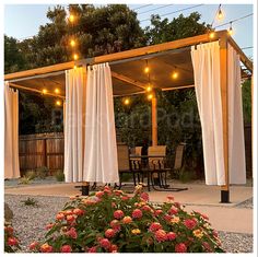 an outdoor patio with curtains and lights on the outside, along with flowers in the foreground