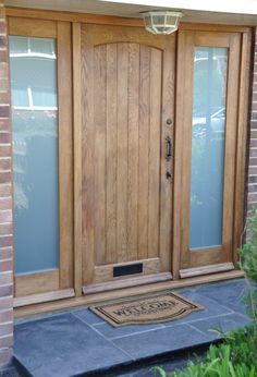 a wooden front door with two sidelights and a welcome mat on the ground in front of it