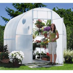 a woman standing in front of a greenhouse with potted plants