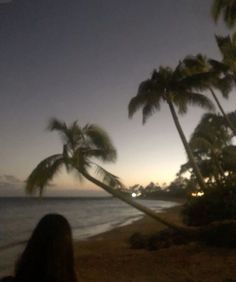 a woman sitting on a hammock looking out at the ocean and palm trees