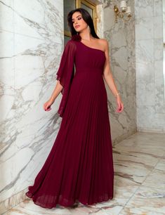 a woman in a long red dress standing next to a marble wall and holding her hand on her hip