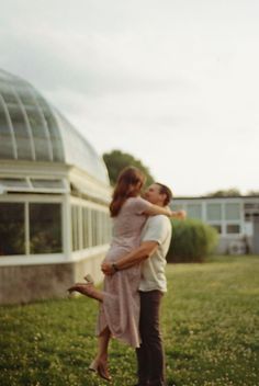 a man and woman embracing in front of a glass house with the sun shining on them