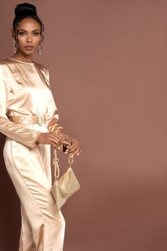 a woman in a gold jumpsuit holding a handbag and posing for the camera