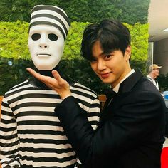 a man standing next to a person with a mask on his face and wearing a striped shirt