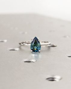 a blue diamond ring sitting on top of a silver surface with drops of water around it