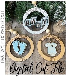 two baby's first christmas ornament hanging on a wooden table next to a pine tree