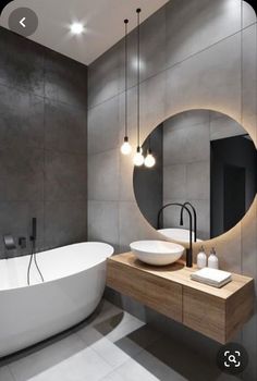 a white bath tub sitting next to a sink in a bathroom under a round mirror