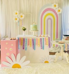 a table with cake, cupcakes and flowers in front of a rainbow backdrop