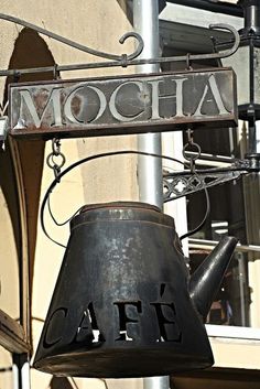 a large metal bell hanging from the side of a building next to a sign that says moocha