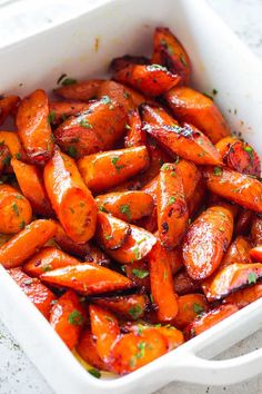 a white dish filled with cooked carrots covered in marinara sauce and parsley