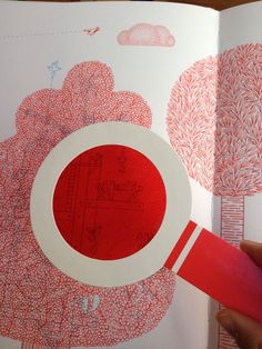 an open book with red and white designs on the pages is being held by a person's hand