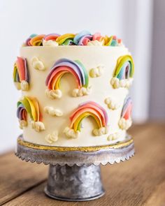 a white cake with rainbows and clouds on it sitting on top of a wooden table