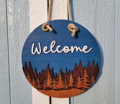 a welcome sign hanging from the side of a wooden door with trees and rope around it