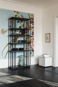 a book shelf in the corner of a room with flowers painted on the wall behind it