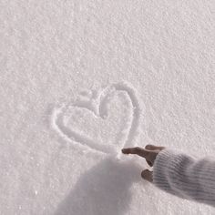 a person's hand is touching the snow with a heart drawn on it