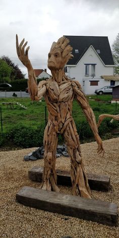 a wooden statue of a grooter holding his hands up in front of a house