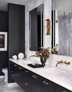 a bathroom with black and white walls, marble counter tops and gold accents on the sinks