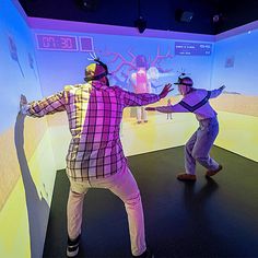 two people are dancing in front of a large screen with an animated image on it