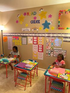 two children sitting at desks in a room with posters on the wall behind them