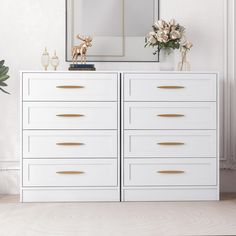 a white dresser with flowers and a mirror on the wall above it in a room