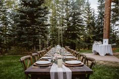 a long table is set with plates and place settings for an outdoor dinner in the woods